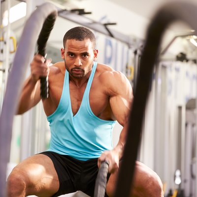 Young man working out with battle ropes at a gym