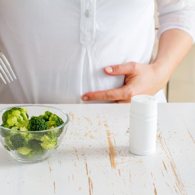 Pregnant female choosing between broccoli in glass bowl and vitamins