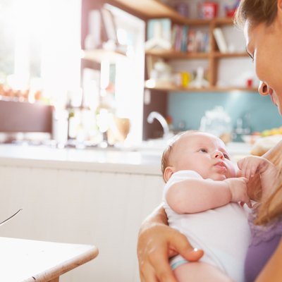 Mother Holding Newborn Baby Daughter At Kitchen Table