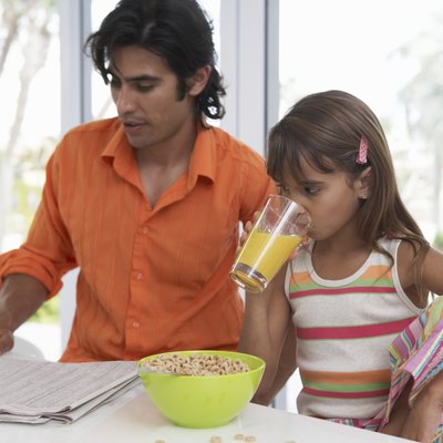 Father reading newspaper sitting with daughter (7-9) having breakfast
