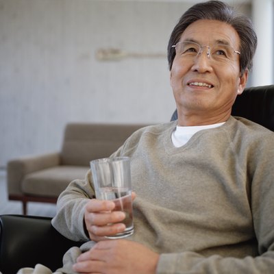Senior man sitting on armchair holding glass of water, looking up