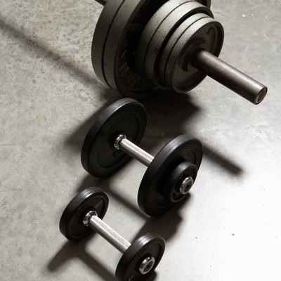 Two dumbbells and barbell side by side on concrete floor