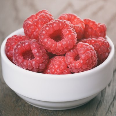 raspberries in white bowl on wood table