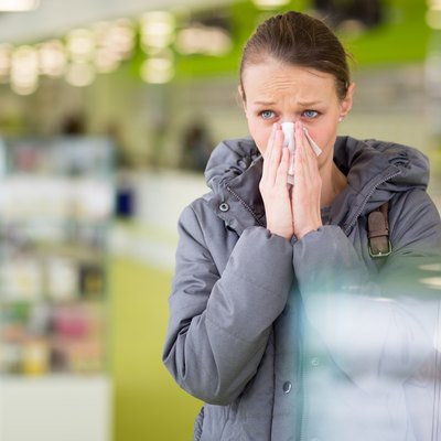 Young woman blowing her nose while in a modern pharmacy