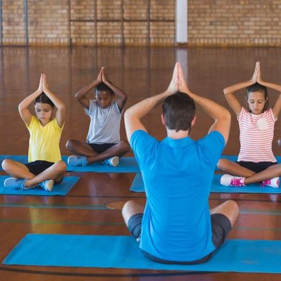School kids and teacher meditating during yoga class in basketball court at school gym