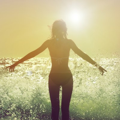 Woman facing the sun with waves crashing at her feet