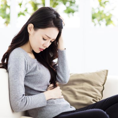 Young woman sitting on sofa and having stomachache