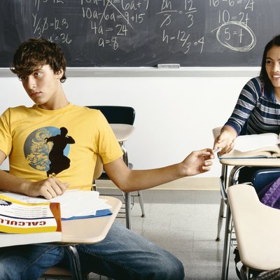 Bored Looking Boy in a Classroom Passing a Note Behind him to a Female Student