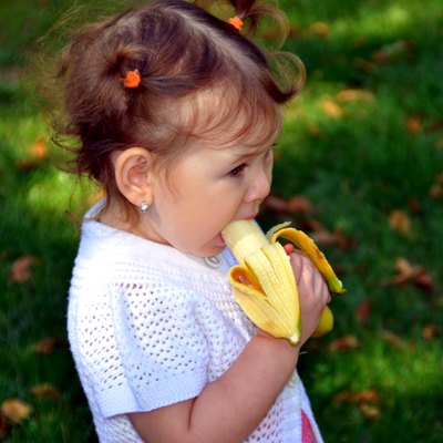 little girl eating a banana in summer outdoors