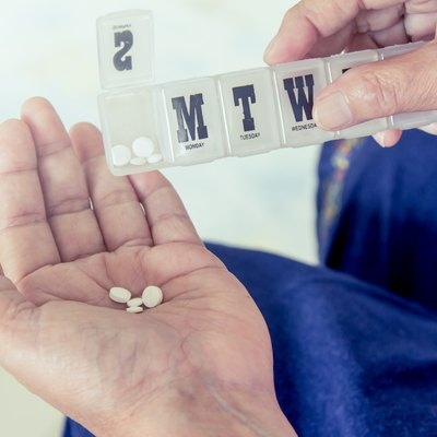 old woman hand pouring pills from a pill reminder box
