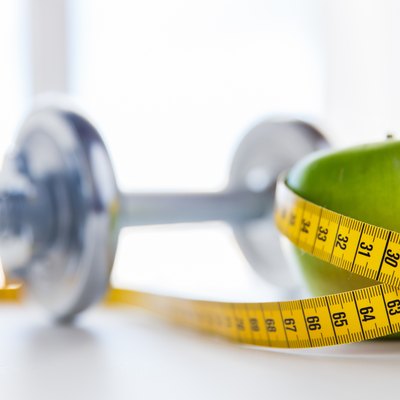 close up of dumbbell and apple with measuring tape