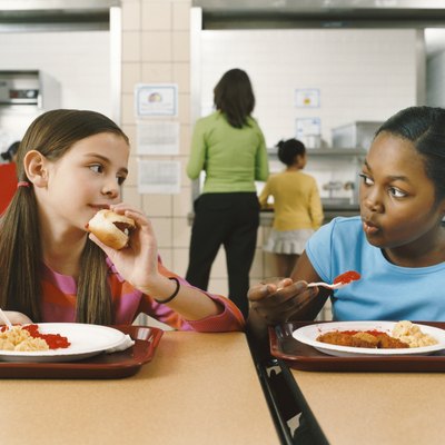 Two Schoolgirls Sitting at a Table in a Canteen Eating Their Lunch