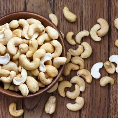 Wooden bowl of cashew nuts from above. On dark wood.