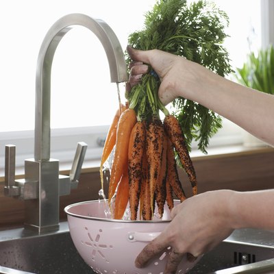 Woman washing carrots at kitchen sink, close-up of hands