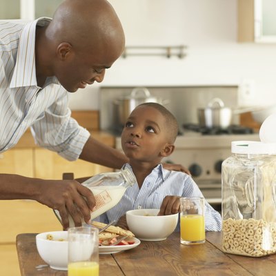 Father pouring milk in bowl for son (5-7) at breakfast table
