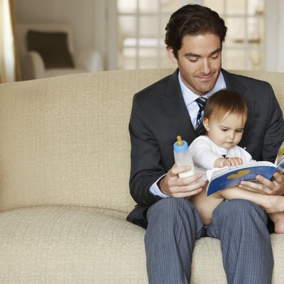 Father reading to daughter (15-18 months) on sofa