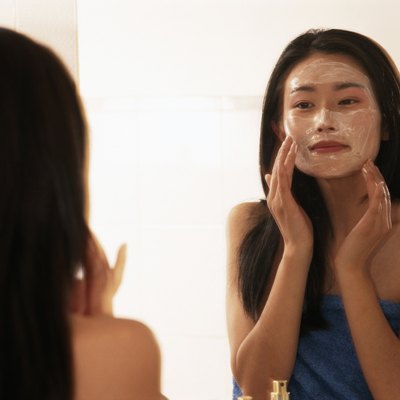 Young woman applying moisturizer on face