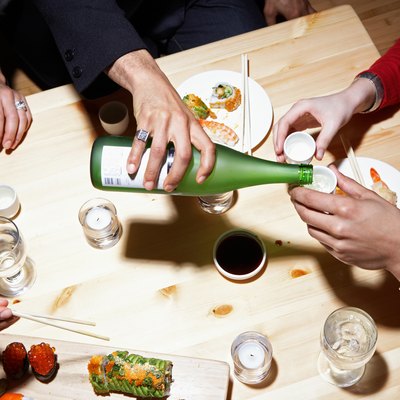 Four adults eating sushi and drinking sake, mid section, elevated view