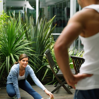 Woman performing leg stretch in garden, man standing in foreground