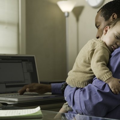 Father using laptop, holding son (9-12 months) on shoulder in home office