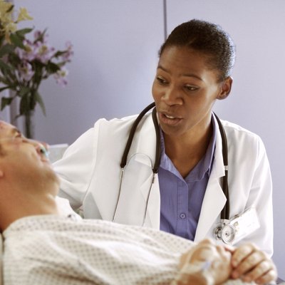 an african american doctor consults with a male caucasian patient as he lies in a hospital bed