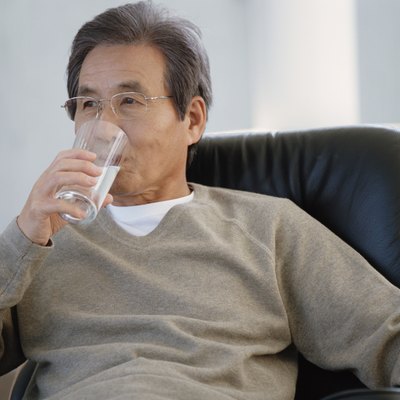 Senior man sitting on armchair drinking glass of water