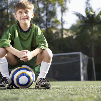 Boy sitting on soccer ball (portrait, low angle view)