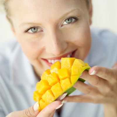 close-up of a woman eating a segmented slice of a mango