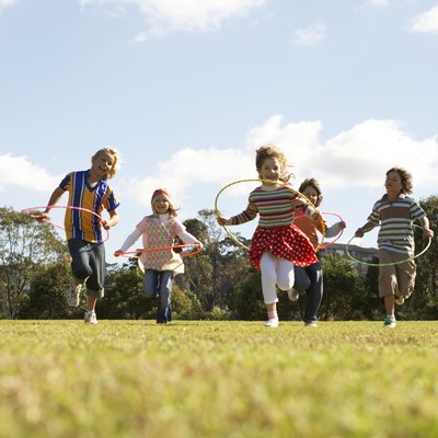 Five children (7-11) running with plastic hoops in park (surface level)