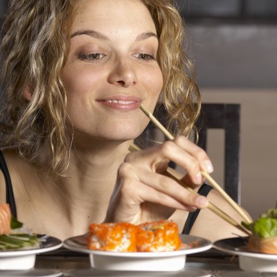 Young woman eating sushi with chopsticks