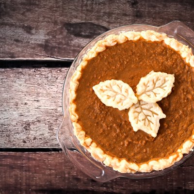 Pumpkin pie with leaf pastry toppings against rustic wood