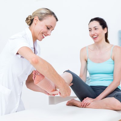 Doctor bandaging her patient ankle