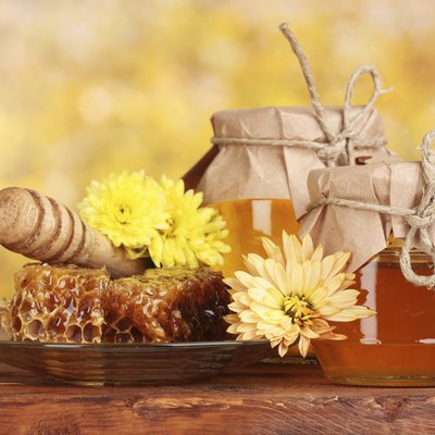 two jars of honey,honeycombs and drizzler on yellow background