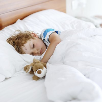 Adorable kid boy after sleeping in white bed with toy