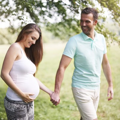 Pregnant woman with husband walking on meadow