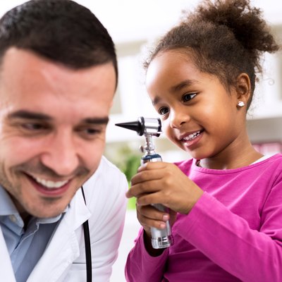 Little african girl holding otoscope and playing with pediatrici