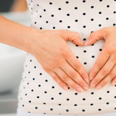 Closeup on young woman holding hands in heart shape on her belly