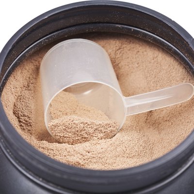 Scoop of chocolate whey isolate protein in black plastic containter