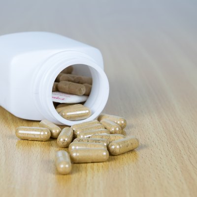 Herb capsule out of a bottle with wood background