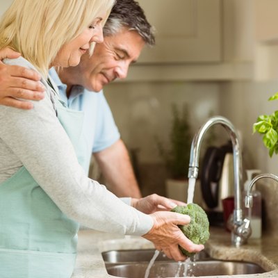 Happy mature couple washing broccoli