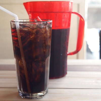glass of cola and red jar on wooden background