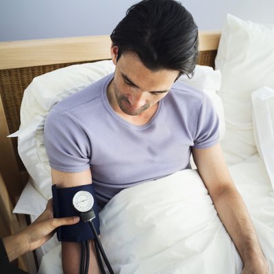Young man lying in bed getting his blood pressure checked
