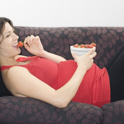 Pregnant woman eating strawberries on sofa