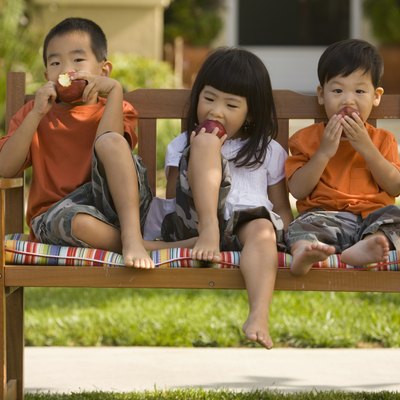 Asian siblings eating apples on bench