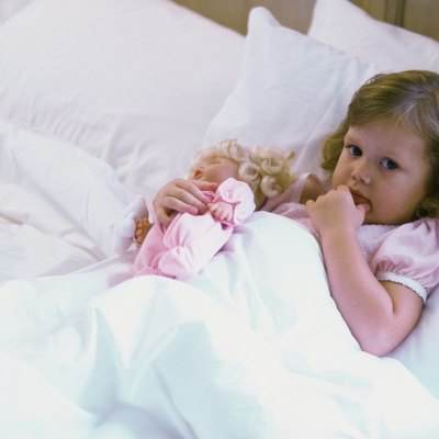 High angle view of a baby girl with a doll lying in bed