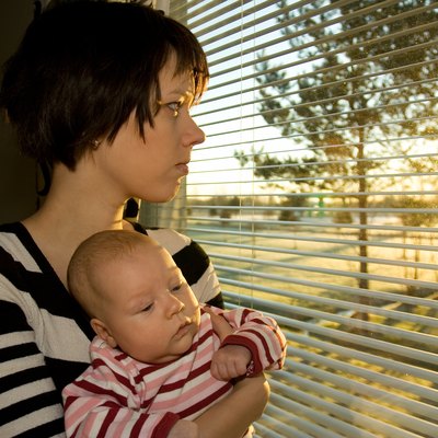 Young mother looking out from the window with her baby 2
