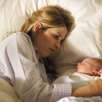 a young caucasian mother lies in the bed alongside her newborn baby