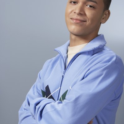 Teenage boy (16-18) against blue background, arms folded, portrait