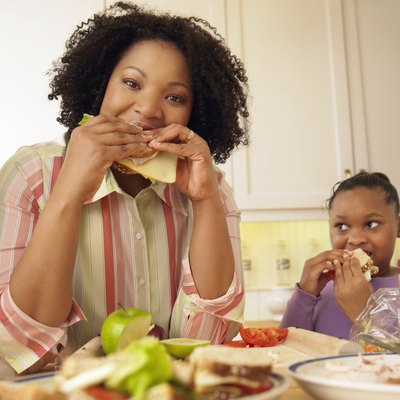 Mother and Her Young Daughter Stand in the Kitchen Eating Cheese Sandwiches for Lunch