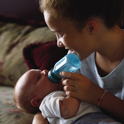 A caucasian older sister bottle feeds her little baby brother